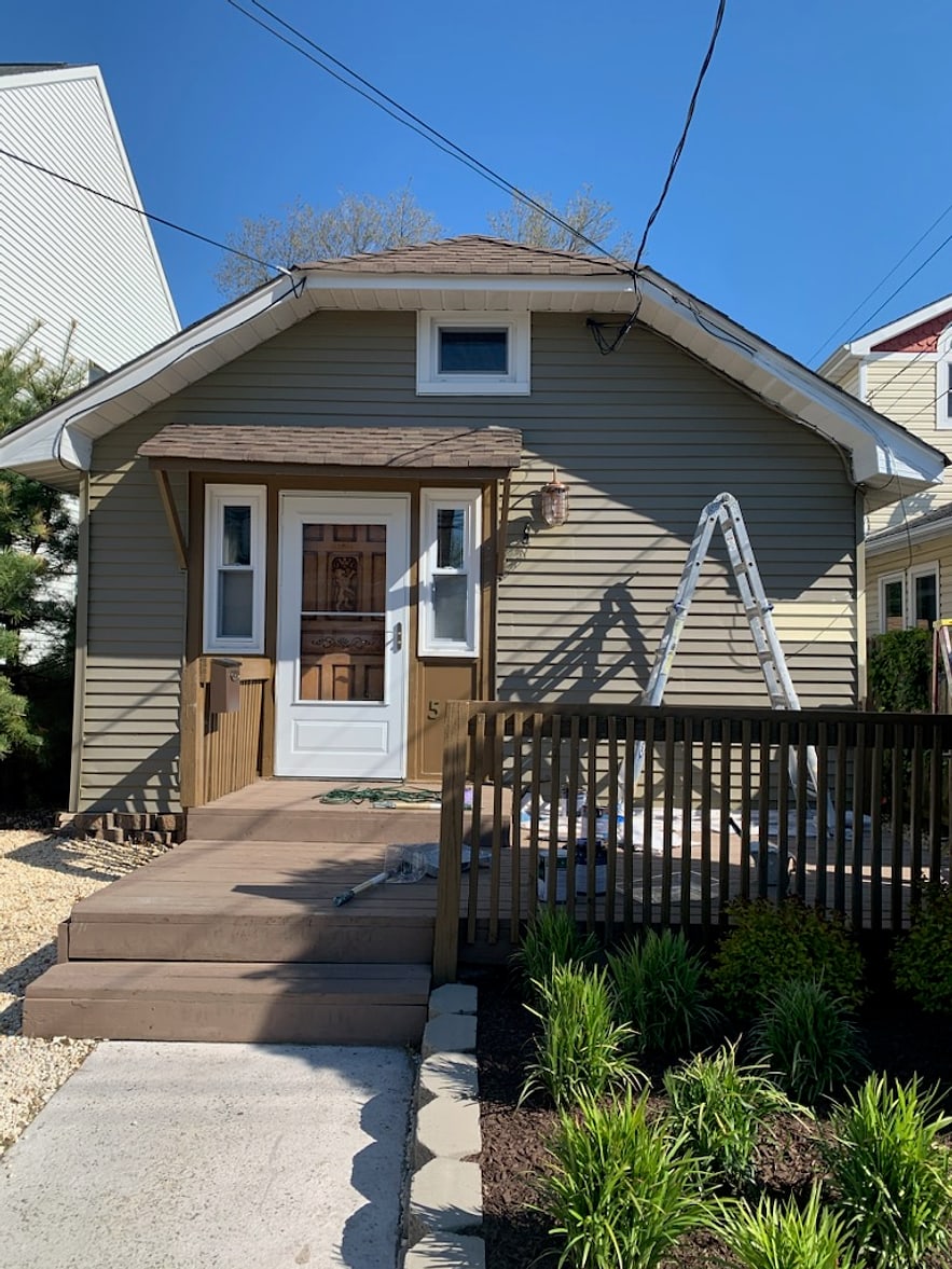 Shore bungalow exterior mid-repaint with ladder on the porch